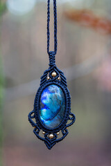 Mineral labradorite gemstone ornamental pendant on blury forest background