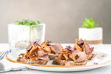 Naklejka na ściany i meble Open sandwiches on rye bread with pickled mushrooms chanterelles and ham on a white plate
