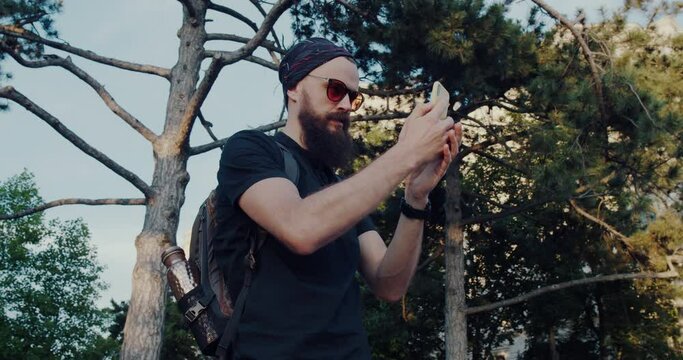 a bearded hipster man and sunglasses take pictures with his phone.