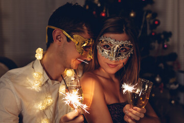 Christmas and New year masquerade party. Couple in love burning sparklers by illuminated Christmas...