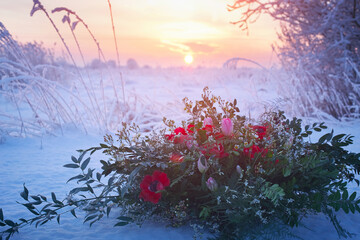 Elegant wedding bouquet of eucalyptus and dark red anemones on the background of snow and sunset
