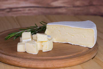 Brie cheese on a wooden board. A sprig of rosemary is behind the pieces of cheese with white mold. Rustic style