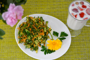 A salad of fresh vegetables is decorated with a nasturtium flower and a glass of milk and strawberries on a green napkin. Vegetable salad for diet food.