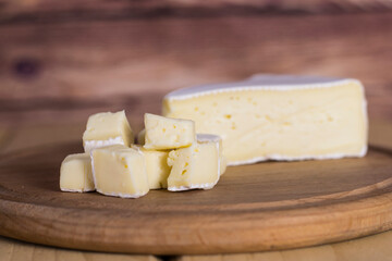 Small pieces of brie cheese on a wooden board against the background of a larger piece. Rustic style, shallow depth of field.