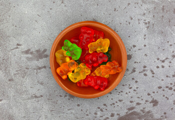 Bowl of colorful gummi bear sugar candies on a gray background top view.