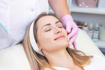 Cosmetological facial massage. beautician doing facial massage to a satisfied beautiful young woman