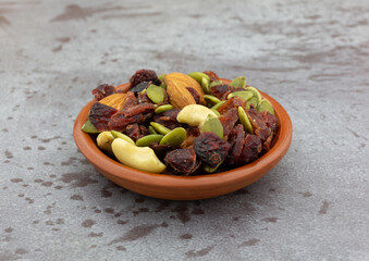 Small bowl filled with seeds, nuts and fruit on a gray background side view.