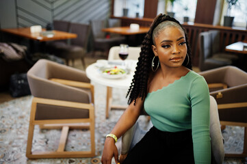 Portrait of attractive young african american woman wearing in green sweater and black jeans pose at restaurant.