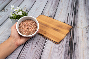 Hands holding 
brown flax seeds on white bowl.
