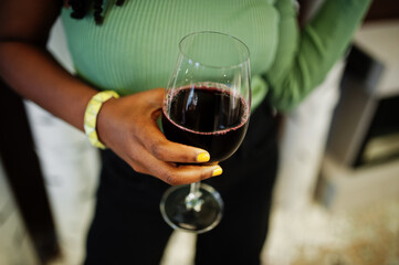 Close up hands of attractive young african american woman wearing in green sweater and black jeans pose at restaurant with glass of red wine.