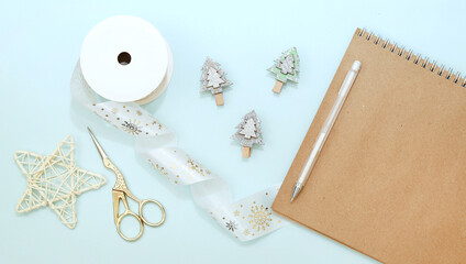 New year and Christmas layout: notebook, pen, golden scissors, decorative ribbon and  clothespins in the shape of Christmas trees on a blue pastel background.