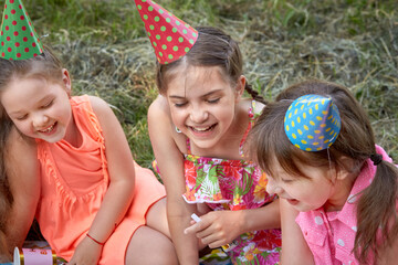 Cute girls in a festive hat, with party whistles and bright dresses. Birthday celebration in...