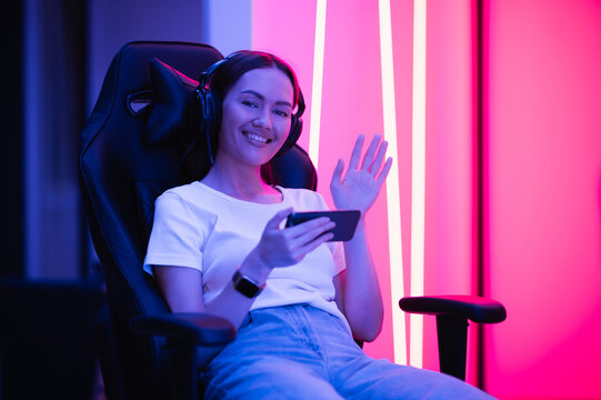 Girl relaxing playing games on mobile phone and sitting on a gaming chair. Room with colorful neon light.