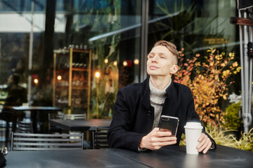 A man is sitting at a table in a cafe on the street Holding a Cup of coffee and chating