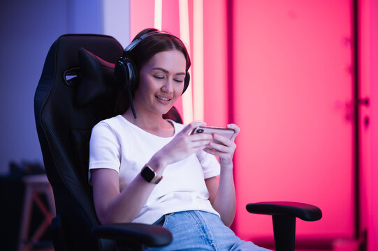 Girl relaxing playing games on mobile phone and sitting on a gaming chair. Room with colorful neon light.
