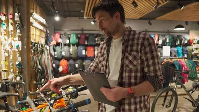 Young Caucasian male seller holding presentation of bicycles goods to buyer, first-person view, professional store of sporting travel goods. Buying equipment and quality service from professionals