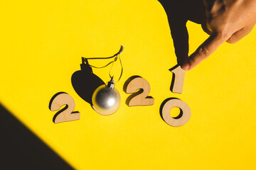 Wooden numbers 2021 chainging 2020 with woman hand and a silver christmas ball on a yellow background. Minimal new year concept.