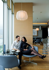 Fashionable adult couple inside cafe with coffee. Man in a white shirt and woman in grey dress looking to each other. Couple sitting in restaurant.