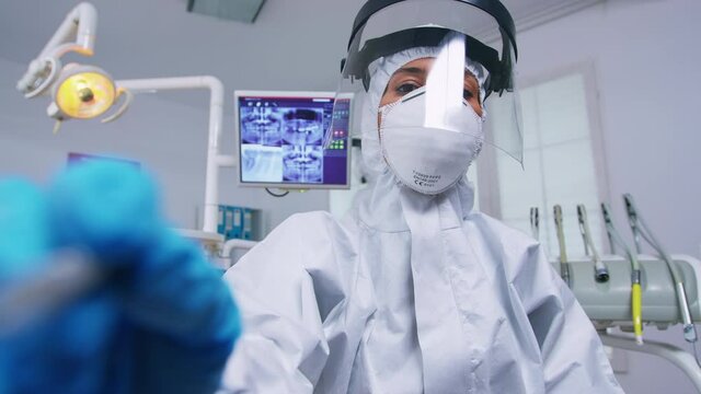 Patient pov while dentist in ppe suit against covid is working on tooth hygine in dental office with new normal. Stomatolog wearing safety gear against coronavirus during heatlhcare check of person.