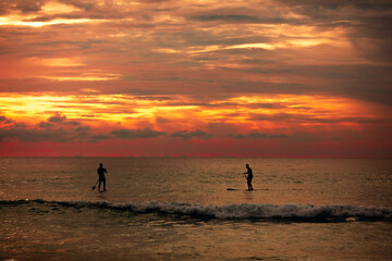 Sea sup surfing under amazing dark sunset sky. Two people on Stand Up Paddle Board. Orange sky. Paddleboarding Concept. Phuket. Thailand.