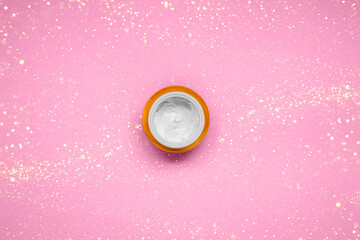 Natural sustainable skin cream on pink backdrop with Christmas glitters - cream texture in container. Flat lay, space for text