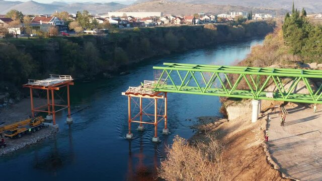 Bridge construction: metal scaffolding used as temporary support for one segment of a small pedestrian bridge. Pair of iron frames on the banks of a narrow river at sunset.