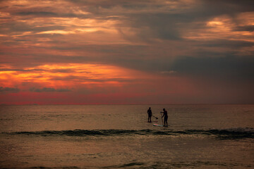 Sea sup surfing under amazing dark sunset sky. Two people on Stand Up Paddle Board. Orange sky. Paddleboarding Concept. trips to warm destinations.  Phuket. Thailand.