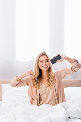  woman showing smartphone with blank screen on bed at home