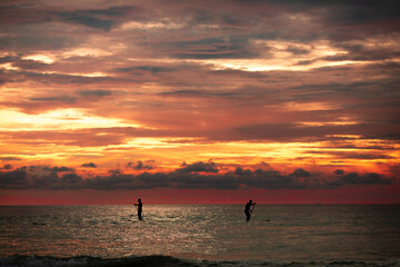 Sea sup surfing under amazing dark sunset sky. Two people on Stand Up Paddle Board. Orange sky. Paddleboarding Concept. Phuket. Thailand.