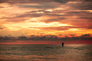 Sea sup surfing under amazing dark sunset sky. Two people on Stand Up Paddle Board. Orange sky. Paddleboarding Concept. Phuket. Thailand.