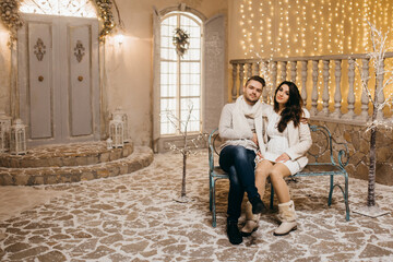 Happy marriage couple sit on bench in winter, cuddling, beautiful wife with loving husband spend holidays, enjoy time together, New Year and Christmas celebration concept