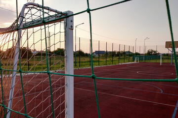 Outdoors mini football and basketball court with ball gate and basket surrounded with high protective fence.