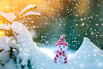 Small funny toy baby snowman in knitted hat and scarf in deep snow outdoors on bright blue and white copy space background. Happy New Year and Merry Christmas greeting card.