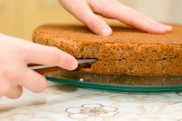 Closeup of female hand holding sharp knife cutting biscuit chocolate cake. Working process of homemade baking.