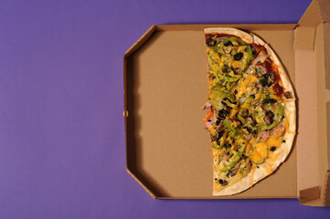 half of pizza in a box on a purple background.