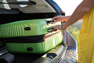 Young woman taking green suitcase from car trunk. Travel and vacations concept.