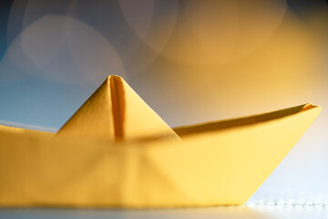 Origami yellow sailing boat on a sea made with blue paper. Paper art style background with ship, ocean and bokeh lights