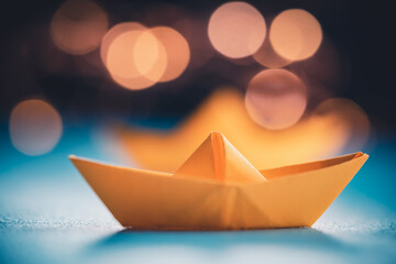 Origami yellow sailing boat on a sea made with blue paper. Paper art style background with ship, ocean and bokeh lights