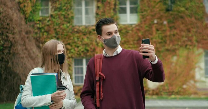 Happy Students in Face Masks Take Selfie by Smartphone Talking Outdoors at High School or University Campus in Autumn. Young Friends Meet Safely with COVID-19 Pandemic Restrictions. 4K Medium Shot