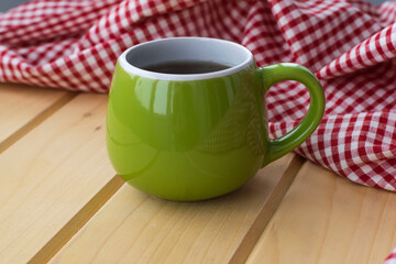 Green cup with tea on a wooden table against the background of a checkered kitchen towel. The...