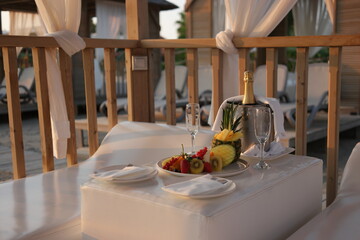 Romantic dinner on the beach. Table with champagne and fruits for two in cozy bungalow. Honeymoon or romantic holidays concept.
