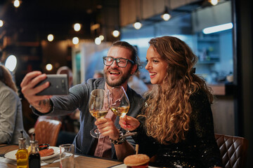 Attractive hipster couple sitting in a restaurant and taking a selfie. It's a diner time.