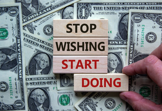Wooden blocks form the words 'stop wishing start doing' on beautiful background from dollar bills. Male hand. Business and start doing concept. Copy space.