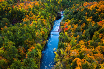 Beautiful travel aerial of a pedestrian foot bridge crossing the bright blue water of the Bad River  at Copper Falls with colorful fall foliage lining the river banks in autumn in Mellen, Wisconsin.