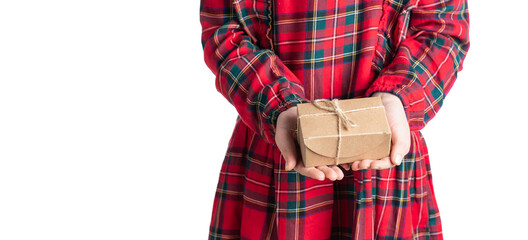 Little girl's hands holding present in brown craft paper box with jute twine bow. Child in red tartan dress, white background, selective focus