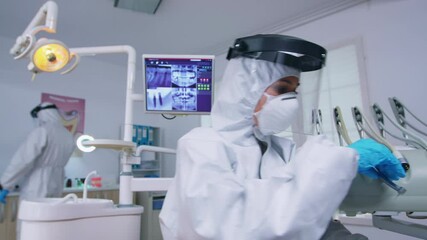 Patient pov of dentist holding dental tools wearing covid protection suit treating patient in new normal clinic. Stomatolog wearing safety gear against coronavirus during heatlhcare check of person.