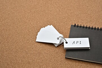 On top of the notebook on the cork board is a wordbook with the word API written on it. It means Application Programming Interface.