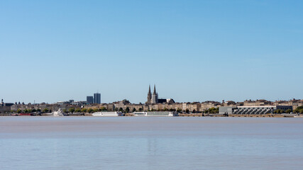 Fototapeta na wymiar View on the Garonne river and city river bank in Bordeaux, a city located in southwestern France. In the background we can see the towers of the cathedral. Sunny day, blue sky.