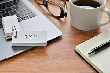 On a desk with a laptop, glasses, coffee, and a notebook, a vocabulary book was placed open There. The word CRM is there. It's an acronym that means Customer Relationship Management.