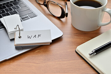 On a desk with a laptop, glasses, coffee, and a notebook, a vocabulary book was placed open There. The word WAF is there. It's an acronym that means Web Application Firewall.